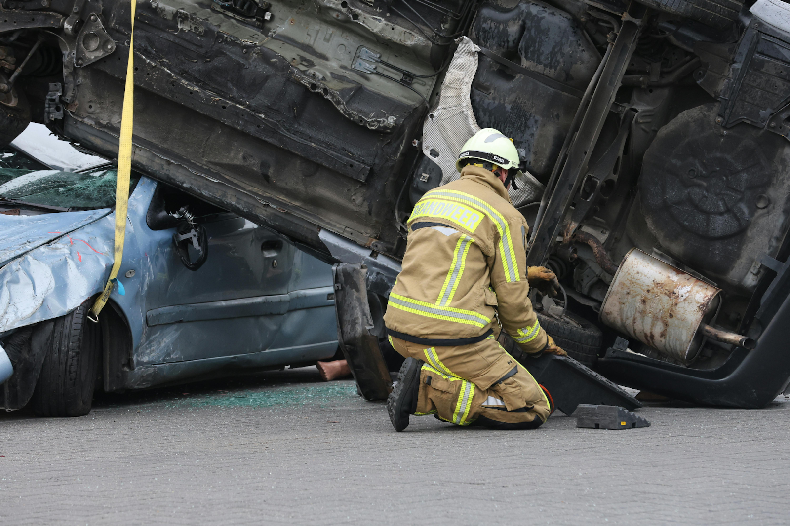 A firefighter kneels beside severely damaged vehicles at a car accident scene.