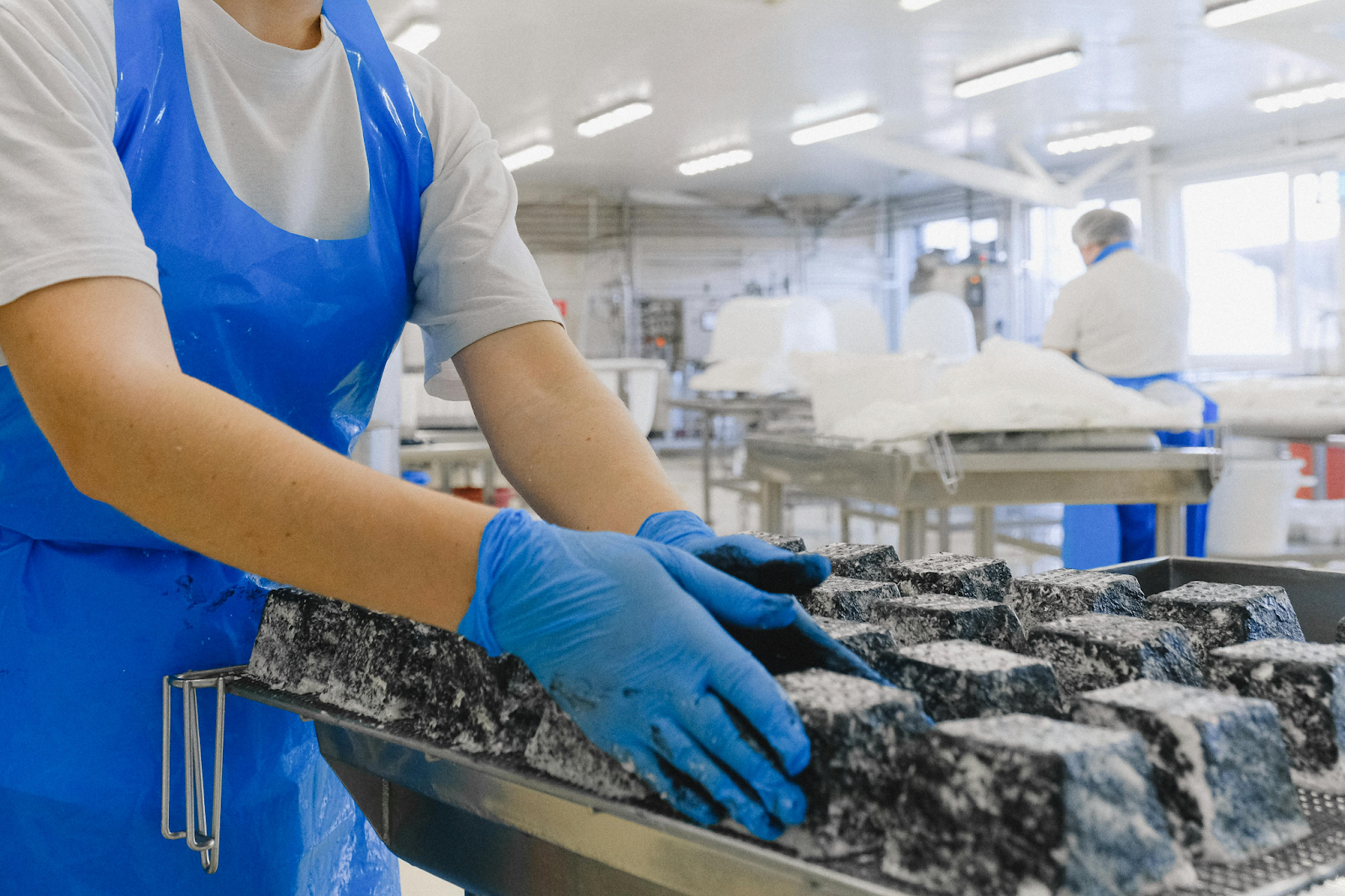 Food production worker performing quality checks on cheese to ensure supplier standards.